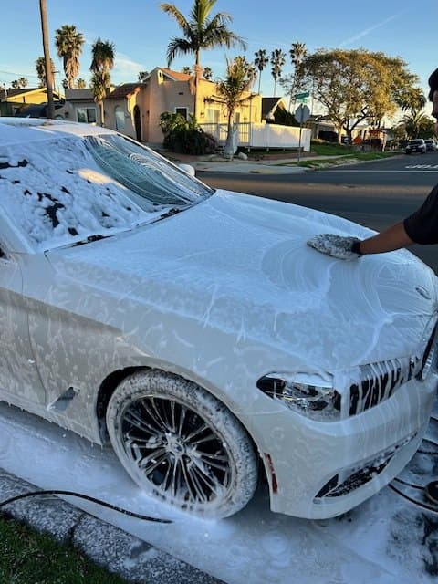 White sedan covered in thick snow-foam during a wash